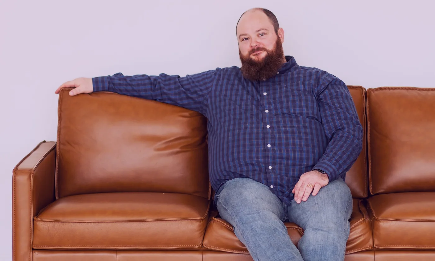 Jordan Smith seated on a tan leather couch for a Ronin Consulting portrait.