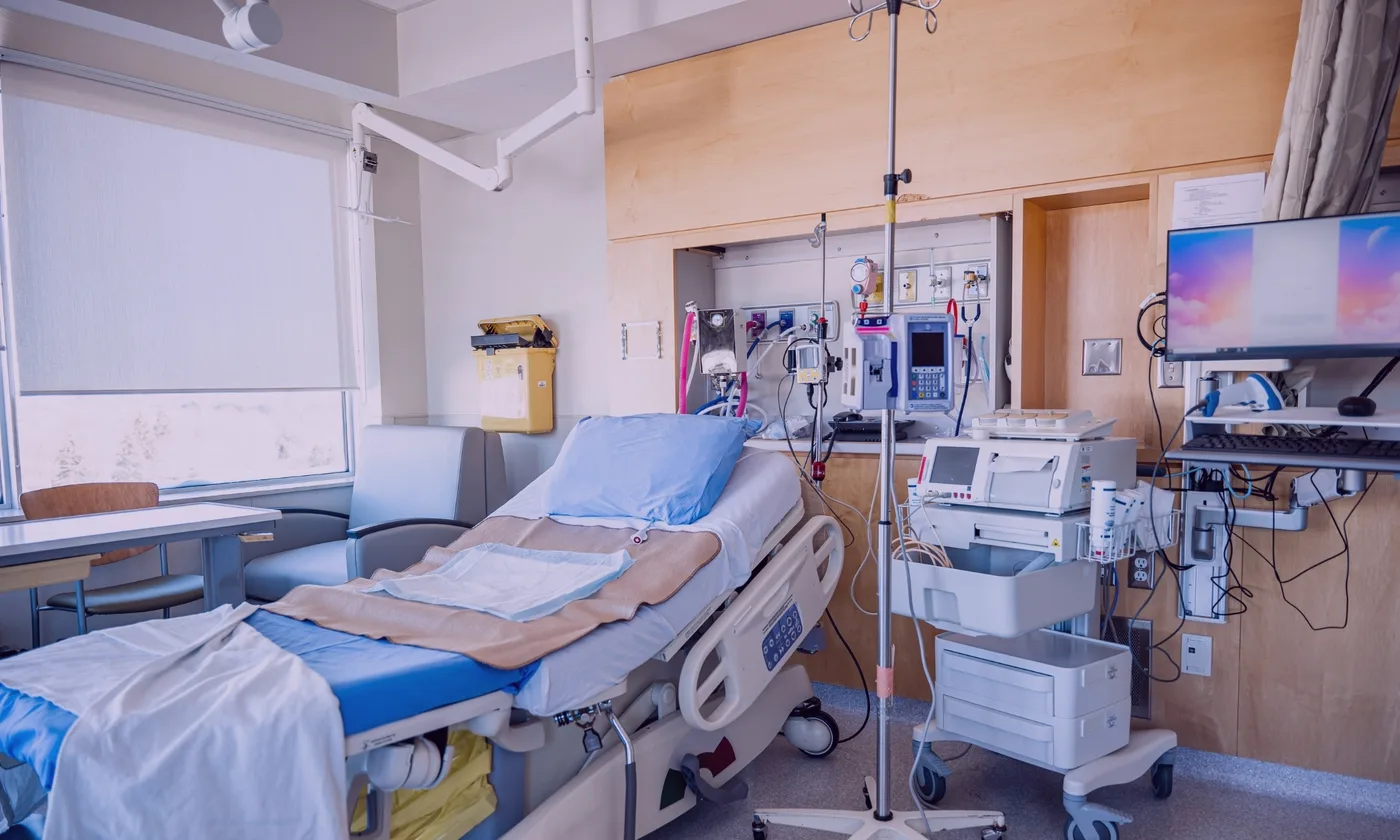 Hospital room with patient bed, monitors, device carts, and clinical technology equipment.
